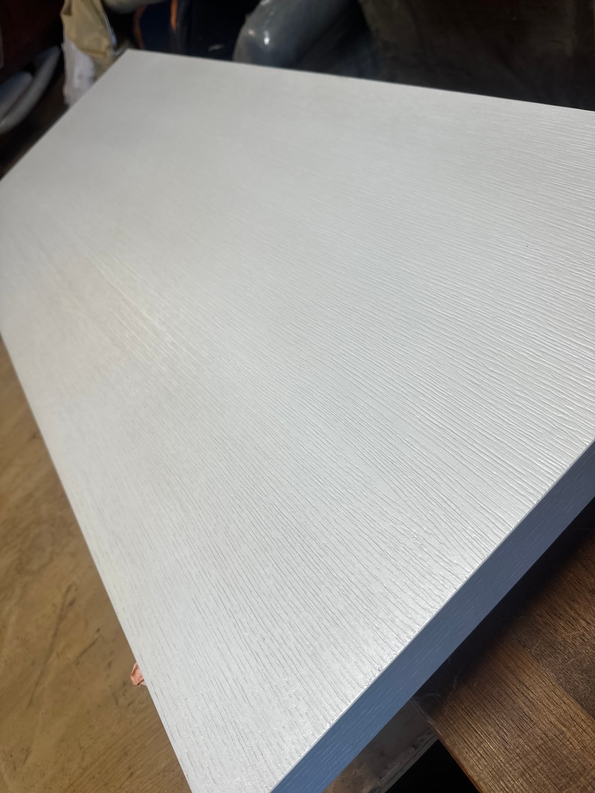 A pale, evenly coated panel with open grain texture resting on a workshop bench